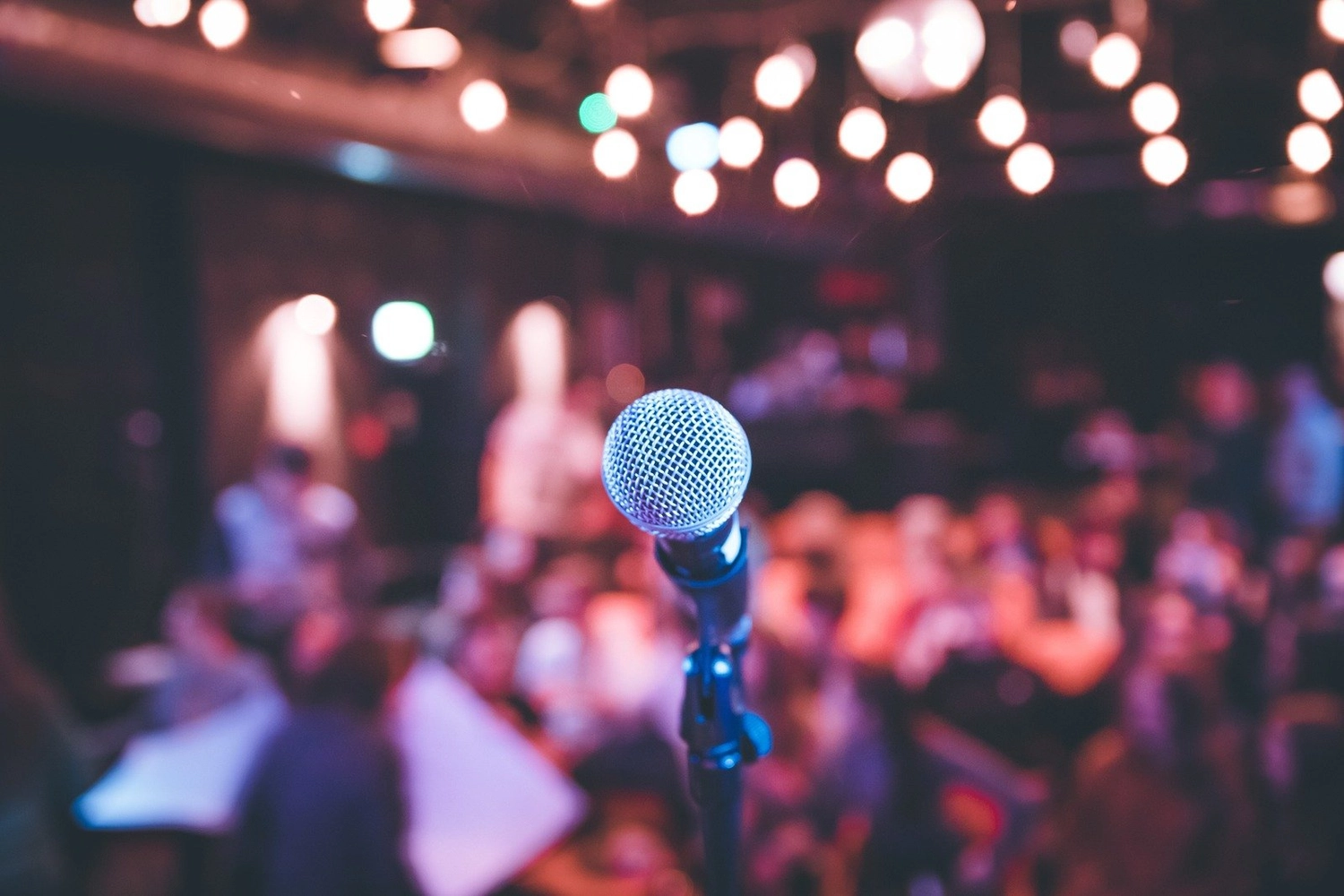 Dela-Noéline Gomado - Zweisprachige Open-Stage-Comedy-Veranstaltung - Ein Nahaufnahme-Foto eines Mikrofons auf einer Bühne, mit einem verschwommenen Publikum im Hintergrund während einer Live-Show.