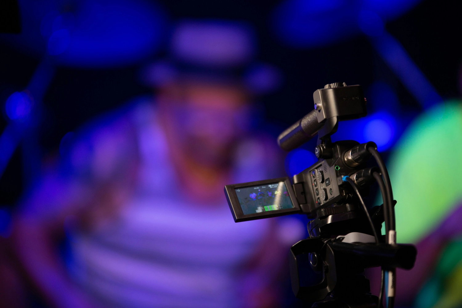 Dela-Noéline Gomado - Zweisprachige Open-Stage-Comedy-Veranstaltung -  Eine professionelle Videokamera mit Mikrofon filmt einen Live-Auftritt in einem Studio mit blauer Beleuchtung.